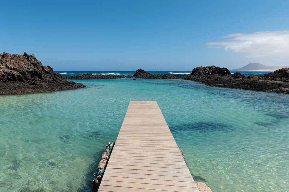 An empty wooden boardwalk leads to a cove of crystal-clear turquoise water