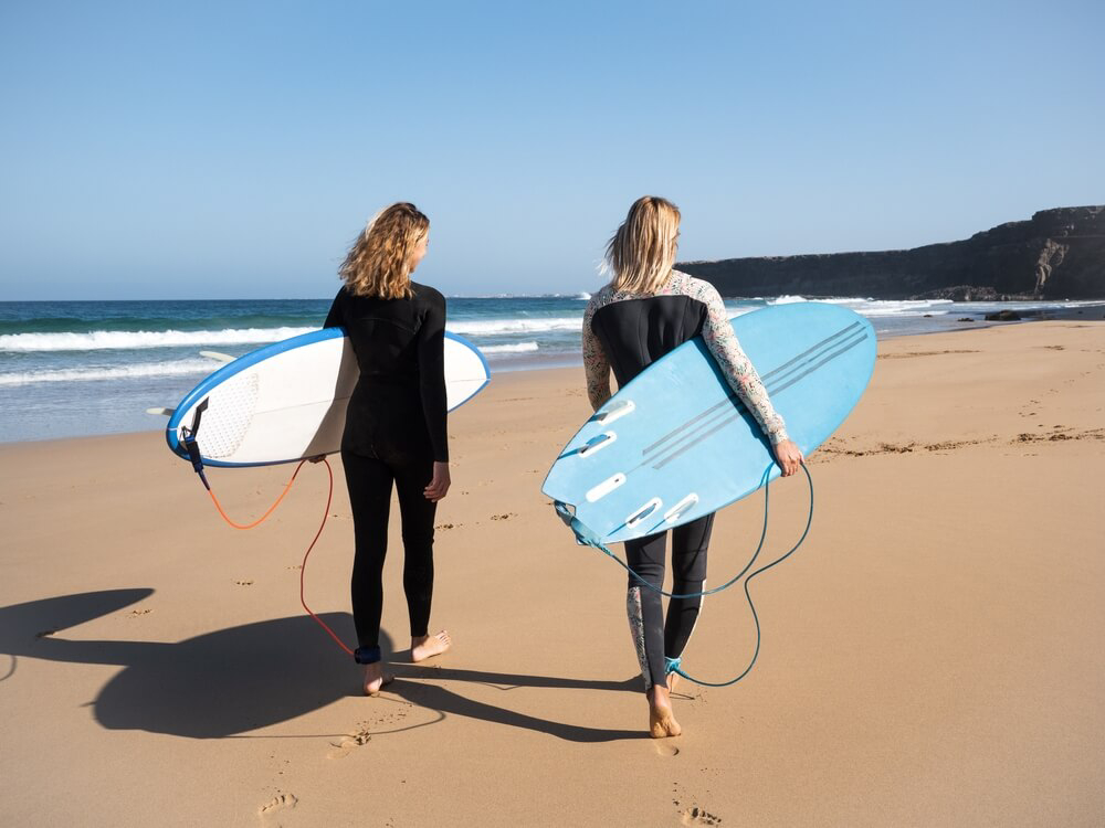 A couple head for the waves dressed in wetsuits and carrying surfboards