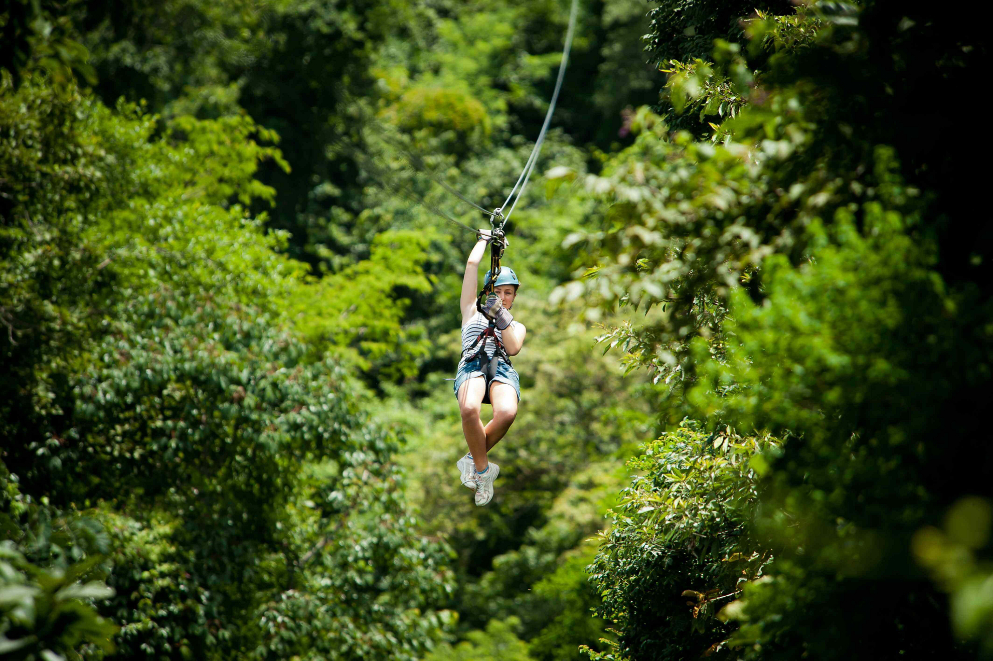 A girl ziplines through the forest doing adventure travel in Costa Rica