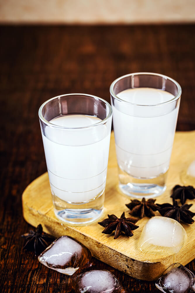 Two small glasses of milky-white mastika spirit on a board decorated with ice and star anise