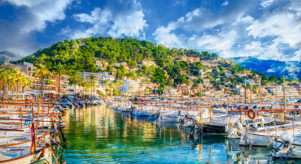 Traditional fishing boats rest before a green hill in Port de Soller harbour