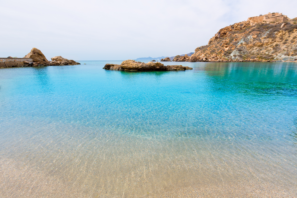A rocky cove with clear turquoise waters surrounded by rugged hills