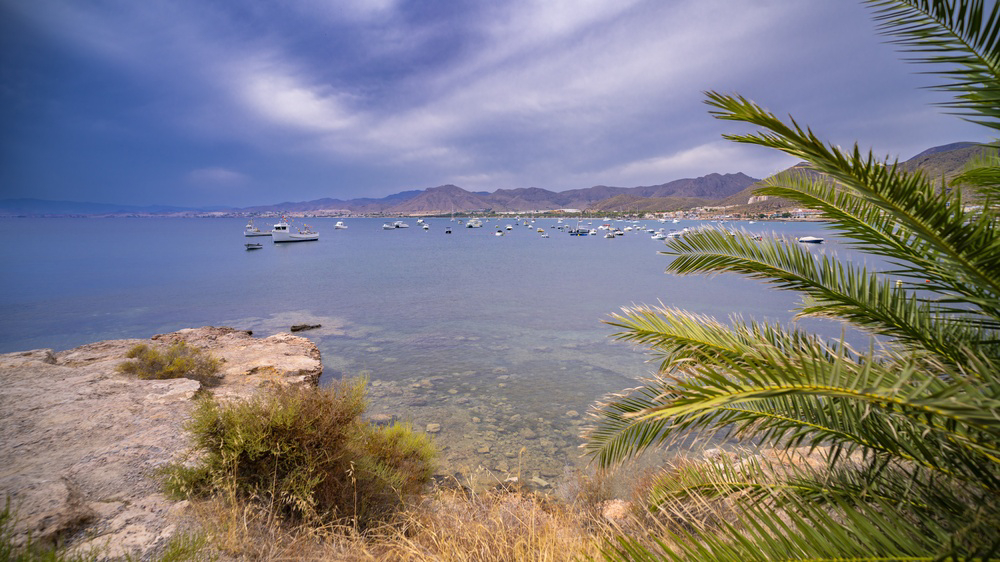 Boats rest in a calm bay backed by rugged mountains