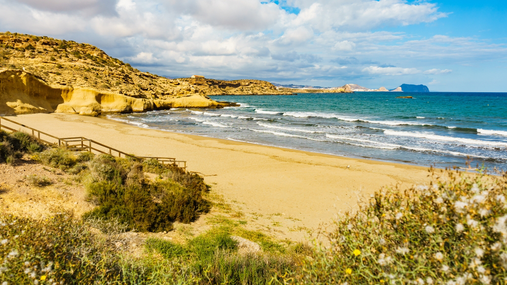 A deserted sandy beach backed by dunes and flanked by cliffs