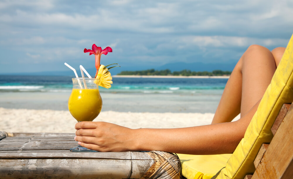 Caribbean cocktails: Woman on beach in a lounger drinking a yellow cocktail