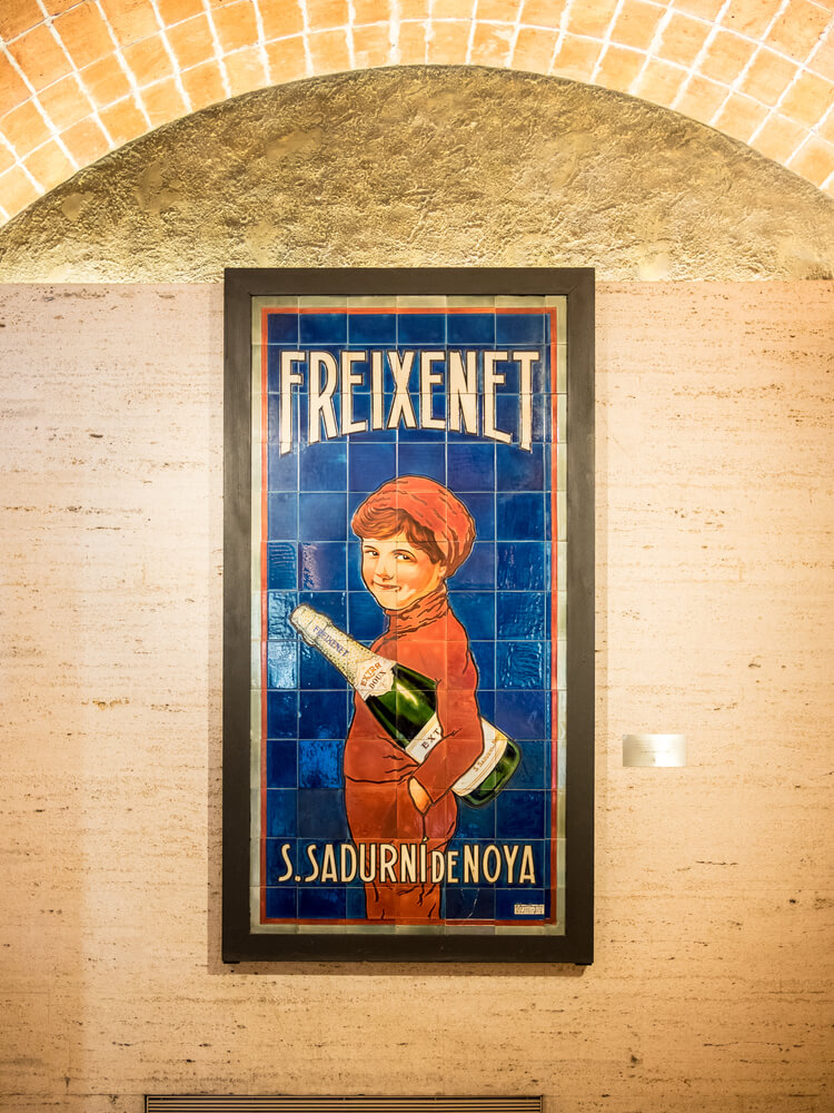 Cava tours in Barcelona: A cream wall with a tiled Freixenet advertising poster