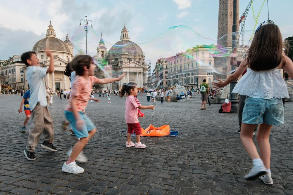 City breaks with kids: children play with bubbles before a street entertainer in Rome