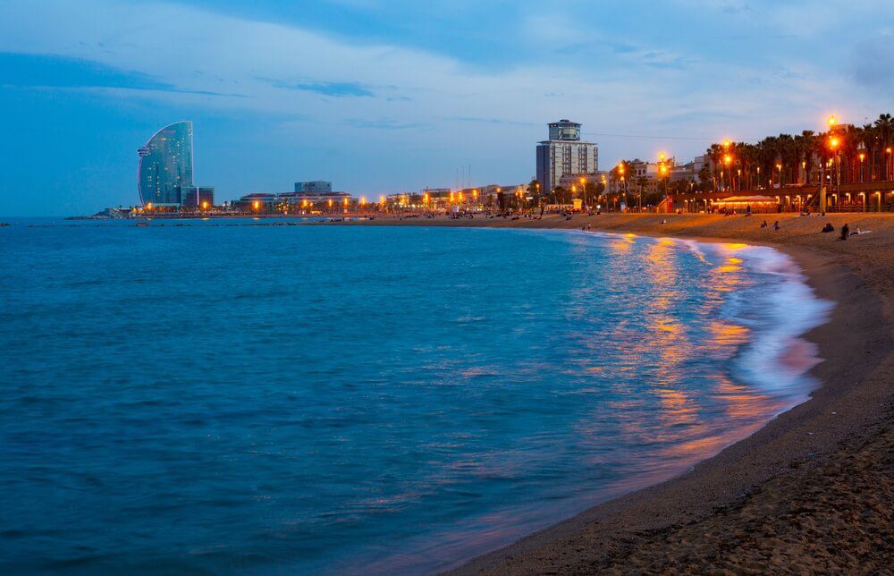Promenade lamps shimmer in the sea at La Barceloneta beach in half-light