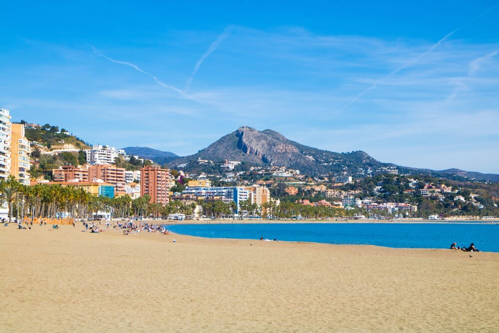 City breaks with beach: a curved beach and blue sea lined with palm trees and hills in the distance