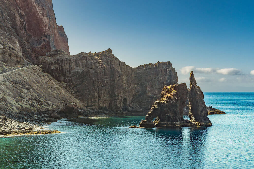 A spectacular rock formation emerges from the sea in front of steep cliffs in El Hierro