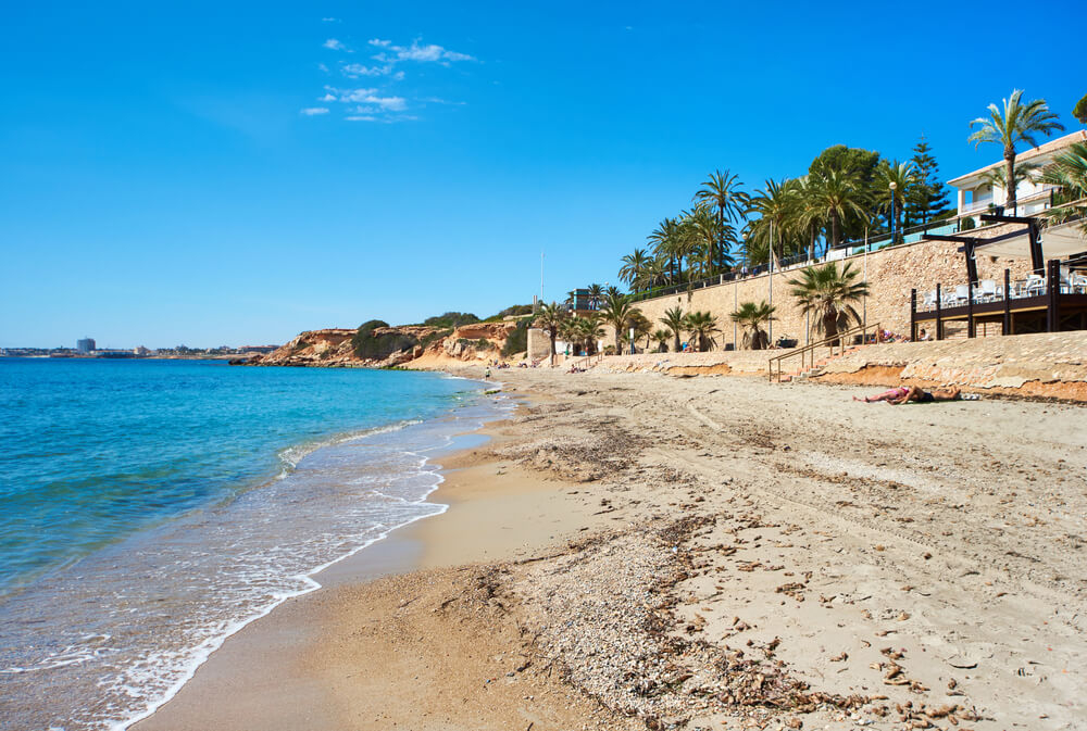 Punta Prima Beach: White sand beach against a sandy city wall