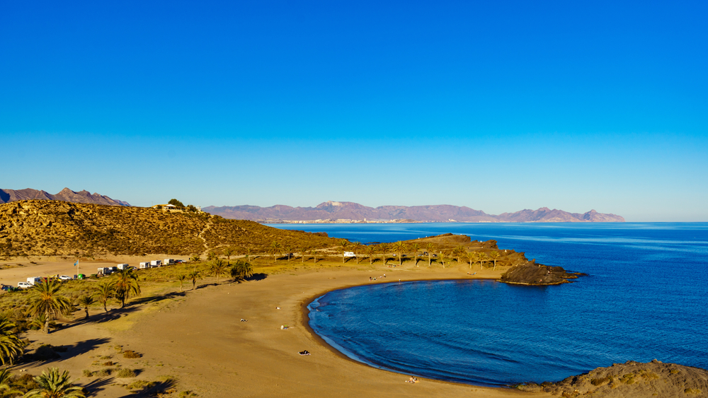 Best beaches in Murcia: a blue sea in a crescent cove against a semi-urban landscape