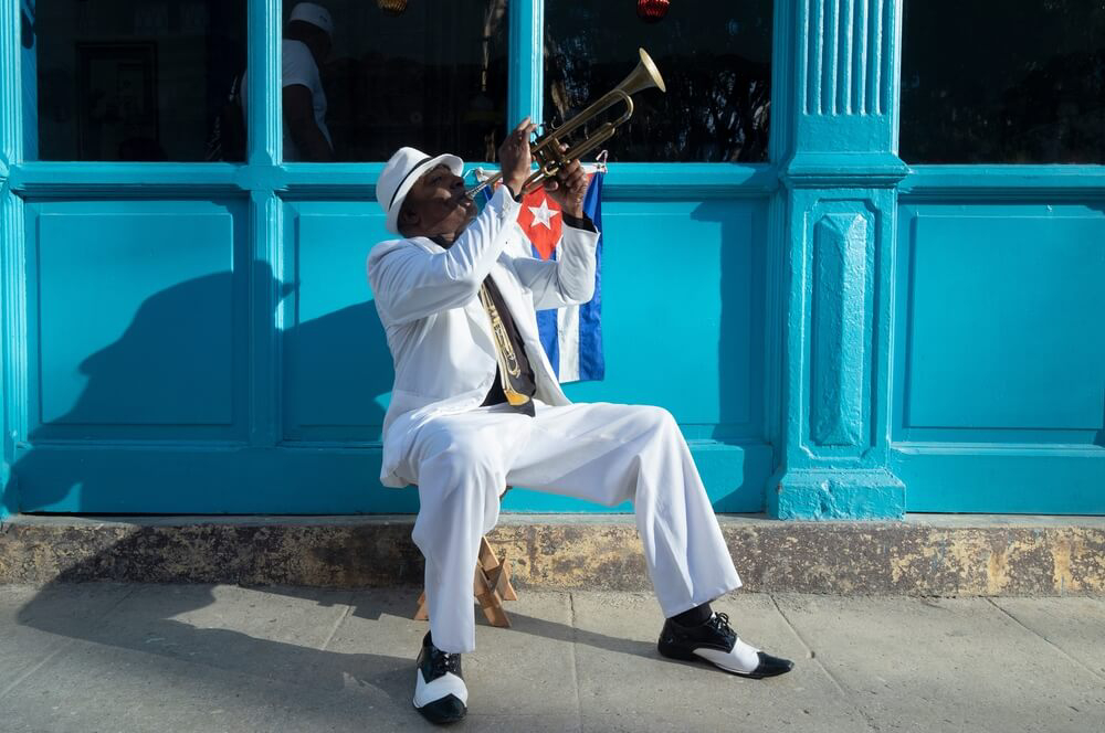 Cuban Culture: A man sitting on the sidewalk playing a trumpet