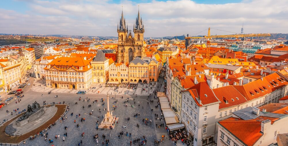 An aerial shot of central Prague featuring a large square and tall spired church