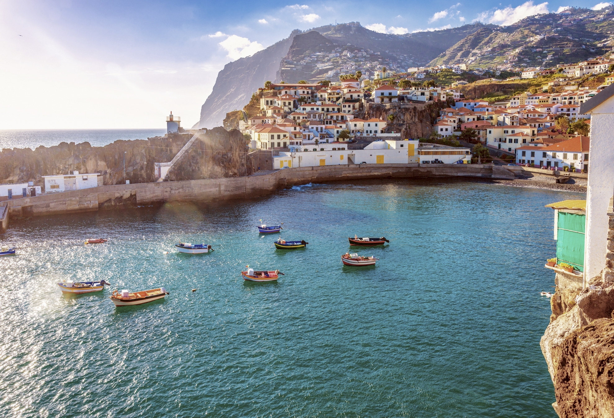 A harbour shelters small fishing boats backed by white houses leading up steep slopes in Madeira