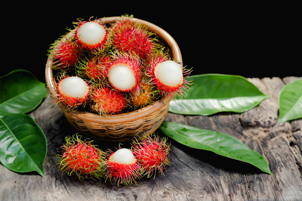 Exotic Fruits: A woven rattan bowl full of rambutan on a wooden surface with green leaves