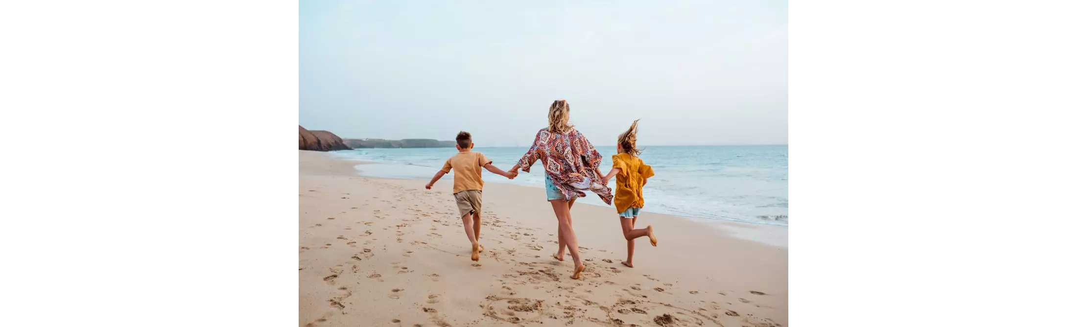 Family holidays in Lanzarote: A blonde haired woman walking hand in hand on the beach with two kids