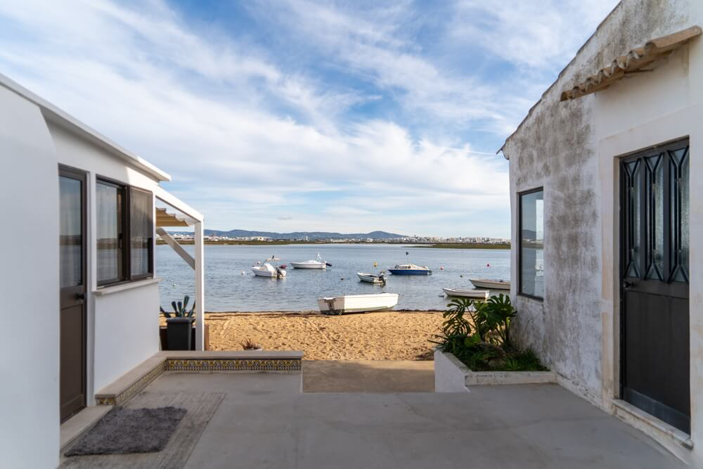 Blick durch zwei Häuser auf einen kleinen Strand mit Booten an der Ria Formosa in Faro.