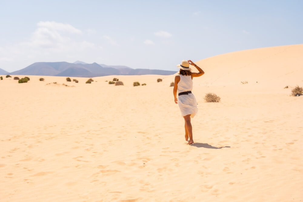 Fuerteventura for couples: a woman walks deserted dunes with volcanic mountains in the distance