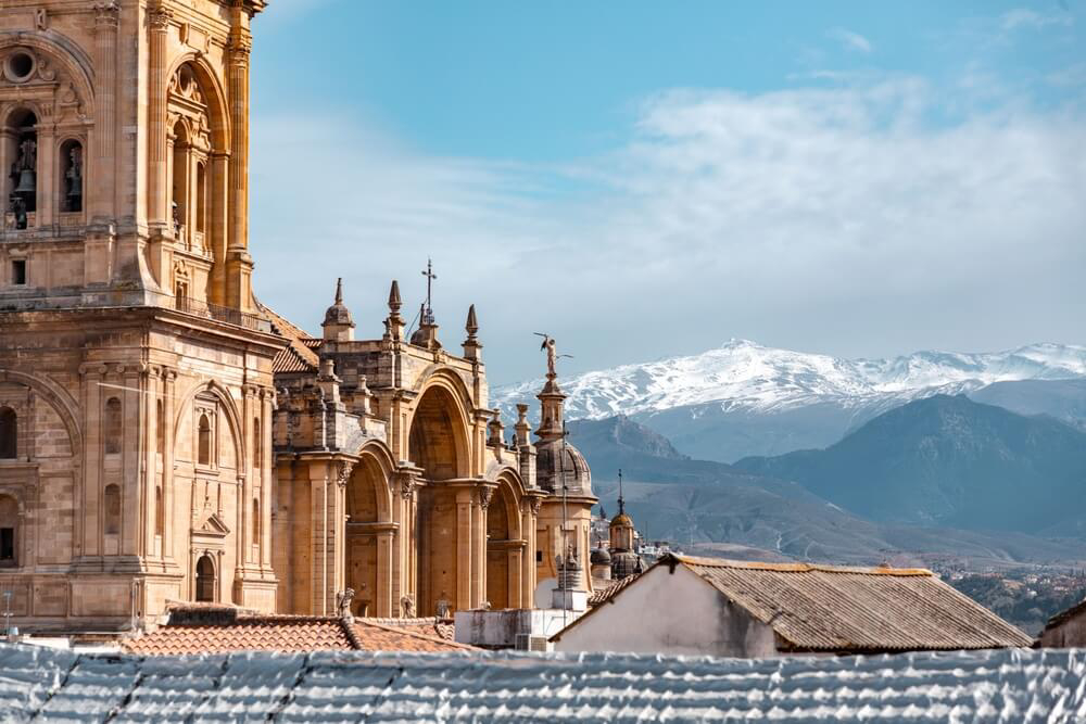 Granada Sehenswürdigkeiten: Kathedrale mit verschneiten Bergen der Sierra Nevada im Hintergrund.