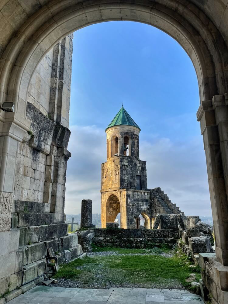 Kutaisi: A grey stone cathedral bell tower with a green turret