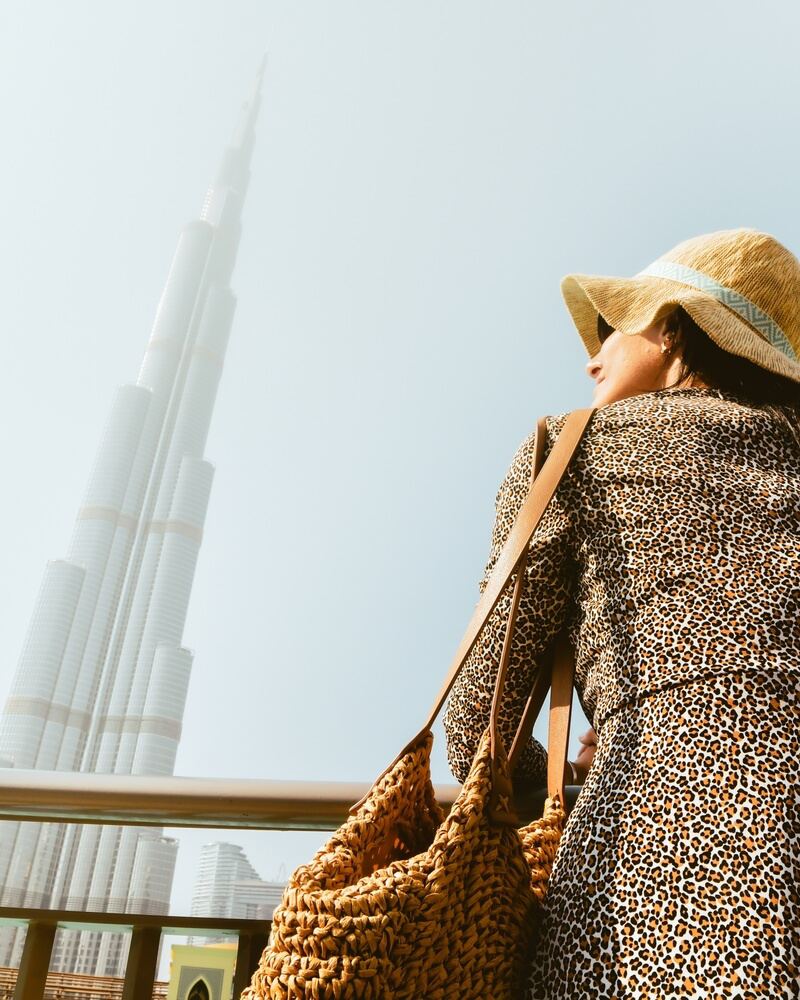 Kleidung in Dubai: Touristin mit bedeckten Ärmeln und Hut vor dem Burj Khalifa.