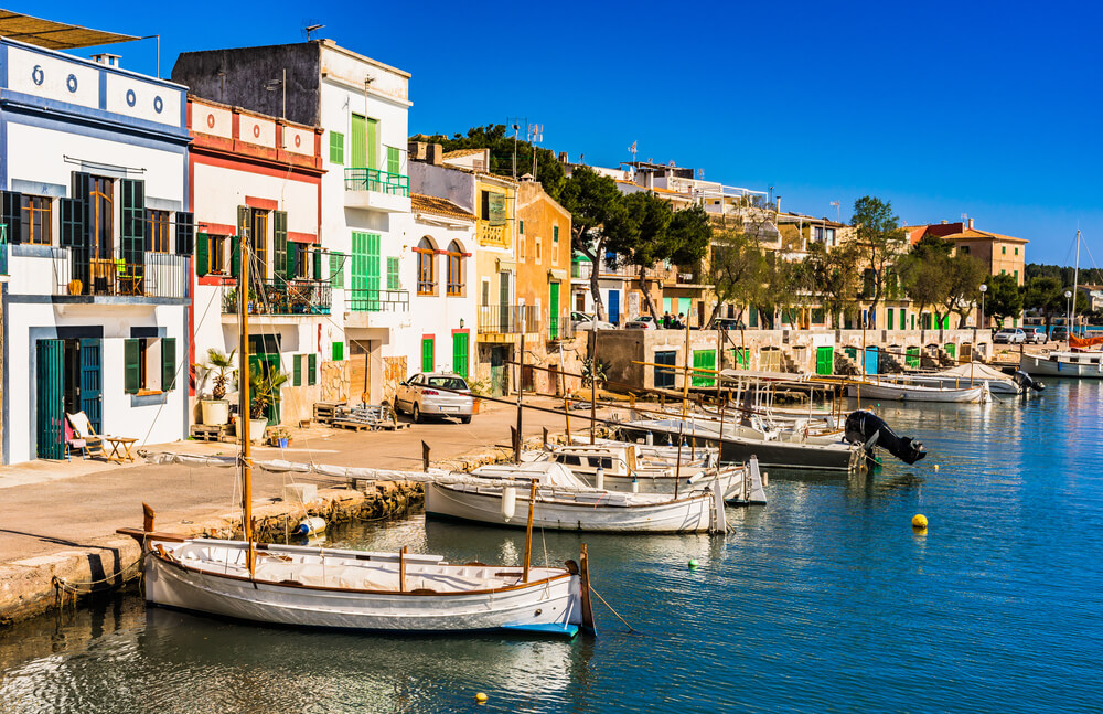 Colourful houses sit by traditional fishing boats on the waterfront in Portocolom