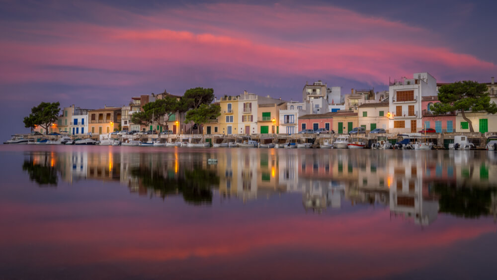 Boats and gaily painted houses reflected in the water in the half-light of Portocolom