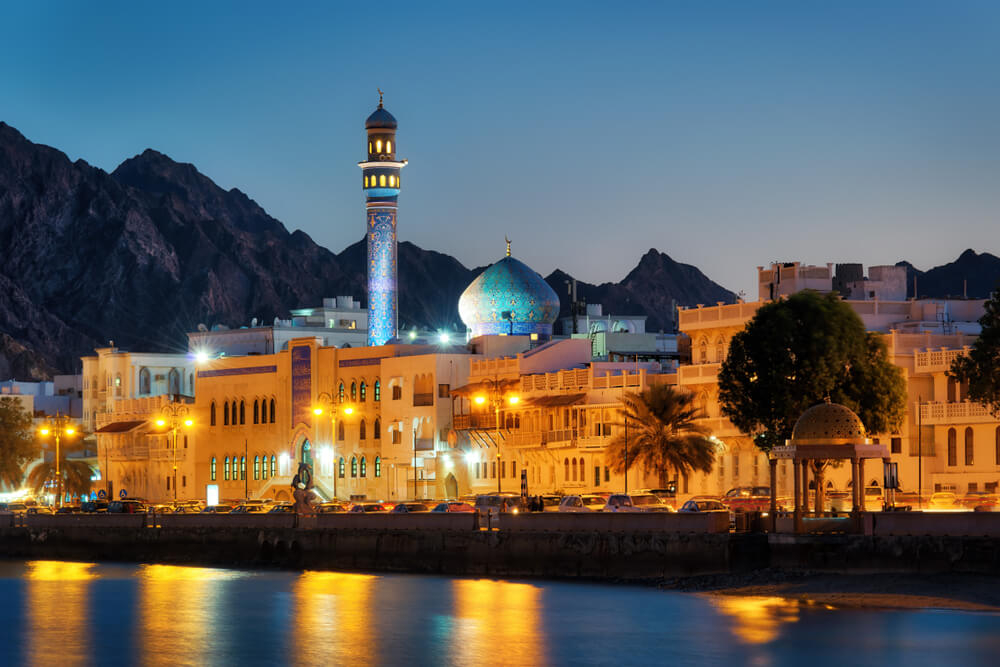 A blue mosque shimmers in the evening light behind Muscat’s waterfront promenade