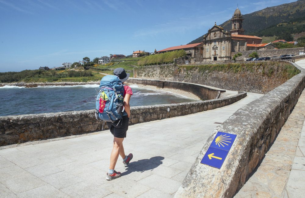 A pilgrim carrying a rucksack heads towards a church along a coastal path