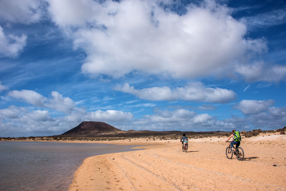 Radfahren auf Lanzarote: Mountainbiker an einem Strand mit einem Berg im Hintergrund