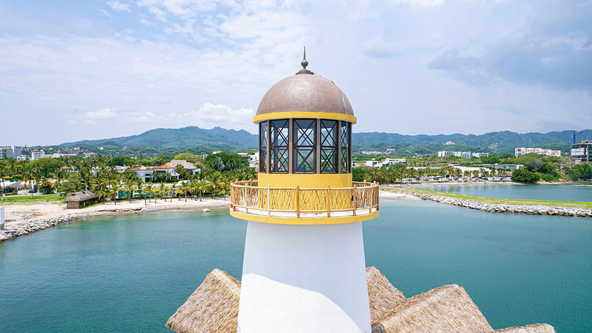 A yellow lighthouse is in the foreground of a Riviera Nayarit landscape