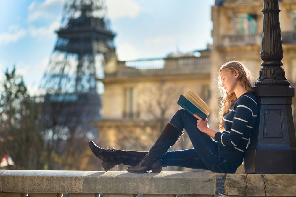Romane für den Urlaub: Frau liest ein Buch mit dem Eiffelturm im Hintergrund