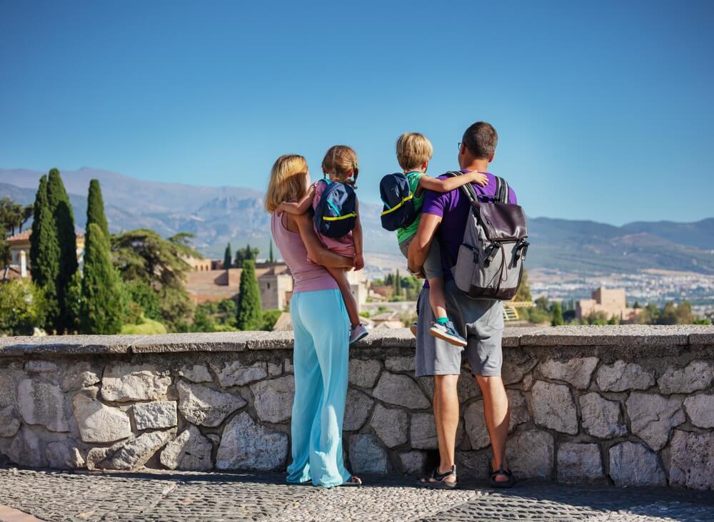 A couple carrying young children view the Alhambra in Granada and the mountains beyond