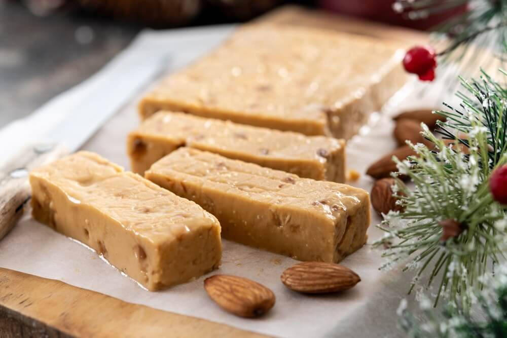 Spanish Christmas Sweets: A wooden board and white paper with brown soft nougat and almonds