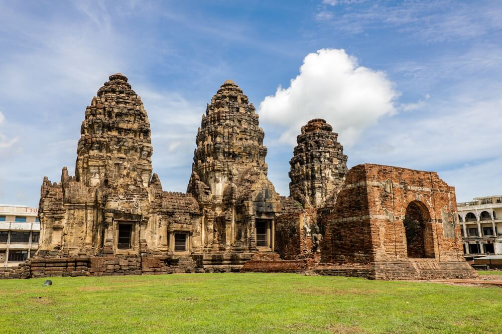 Wat Phra Prang Sam Yot: A red brick and stone temple ruin set on a grass site