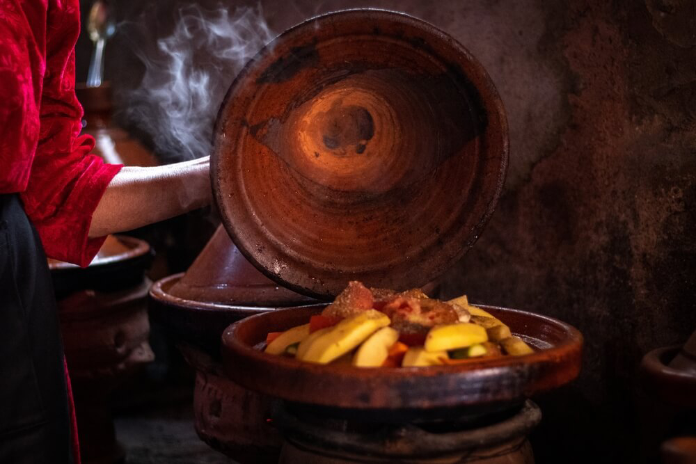 Tagine: A person lifting the lid off a big clay tagine pot
