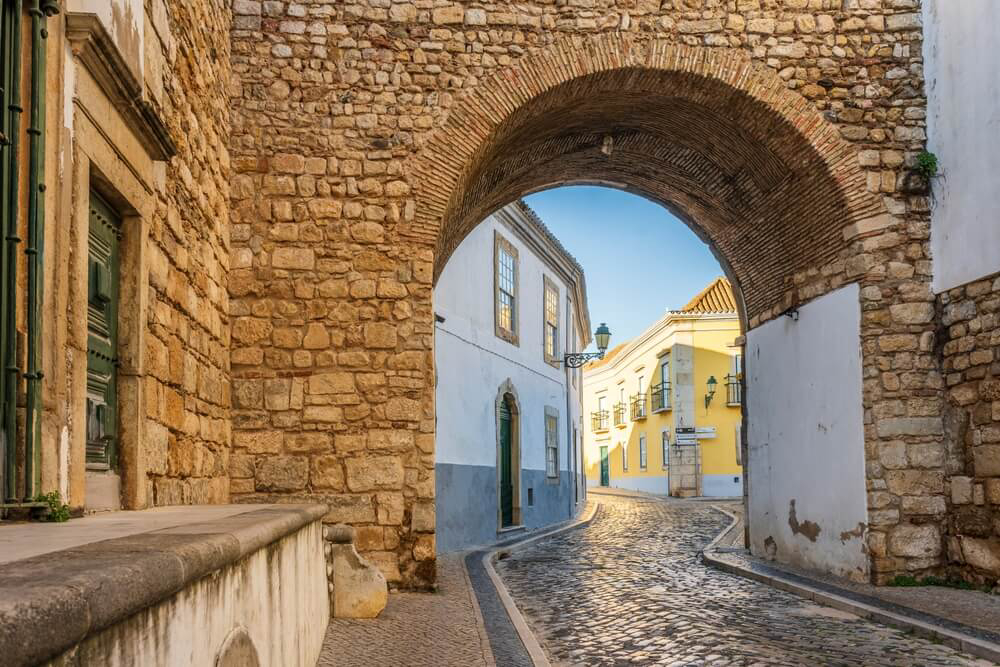 Things to do in Faro: A cobbled street framed by a brick arch and a traditional building