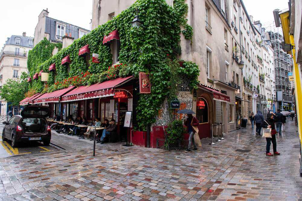 Things to do in Le Marais: A stone building with a red awning and a café terrace 