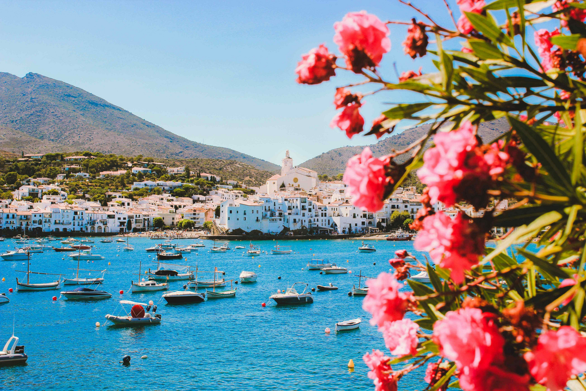 Things to do in the Costa Brava: Views of a white town over the sea with pink flowers