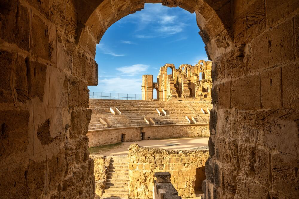 A stone arch framing the Roman amphitheatre of El Jem