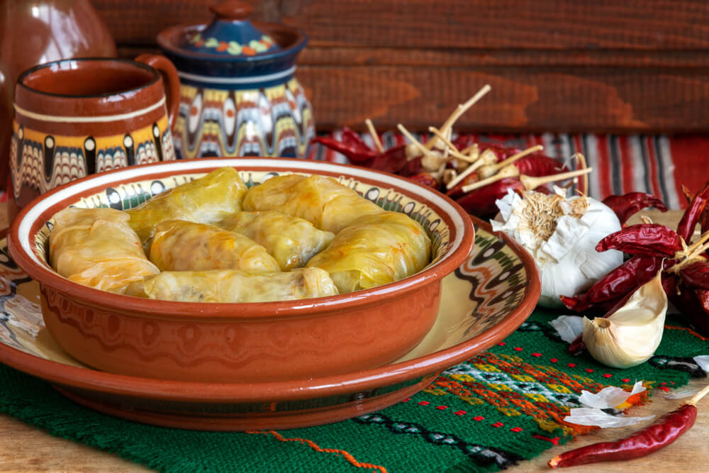 An earthenware dish of stuffed cabbage leaves flanked by garlic and dried red peppers