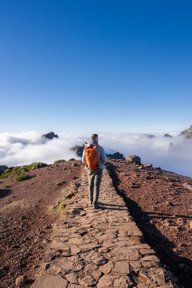 Wandern auf Madeira: ein Wanderer auf einem Steinweg über einem Meer aus Wolken