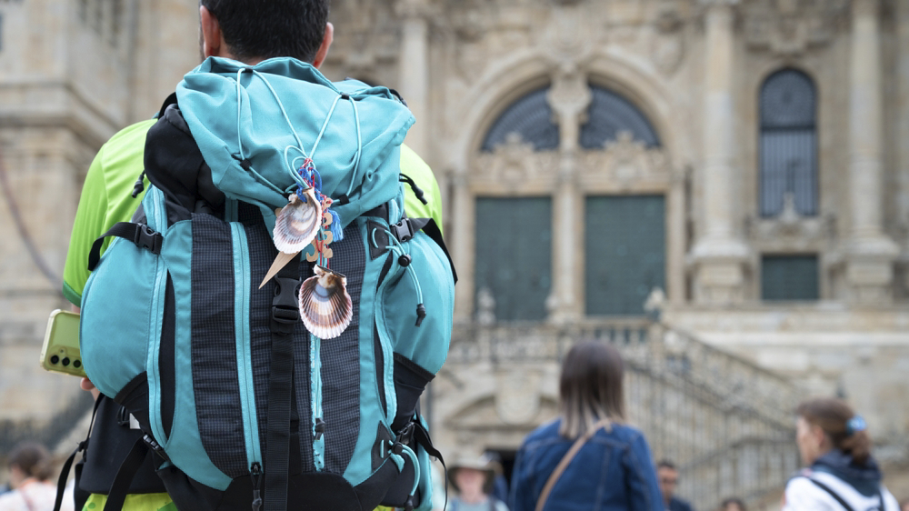 A pilgrim carrying a rucksack stands before a church