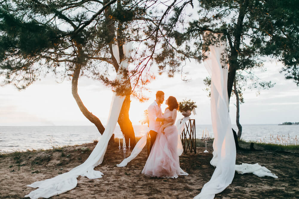 Wedding destinations: A couple on a white beach with trees and a decorated arch