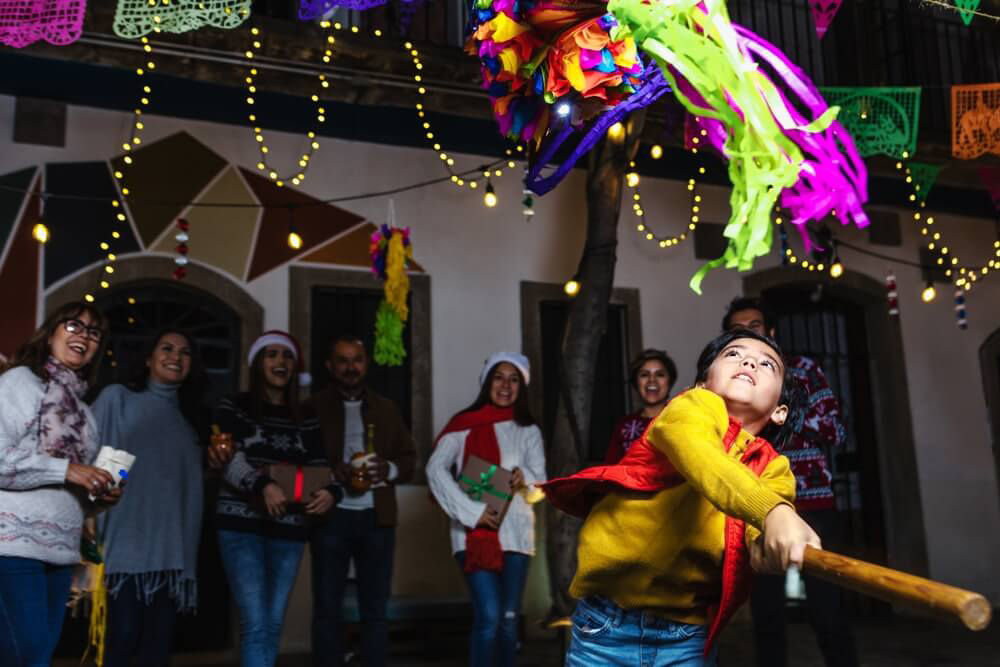 Weihnachten in Mittelamerika: Junge schlägt mit einem Stock auf eine bunte Piñata, Gäste schauen zu