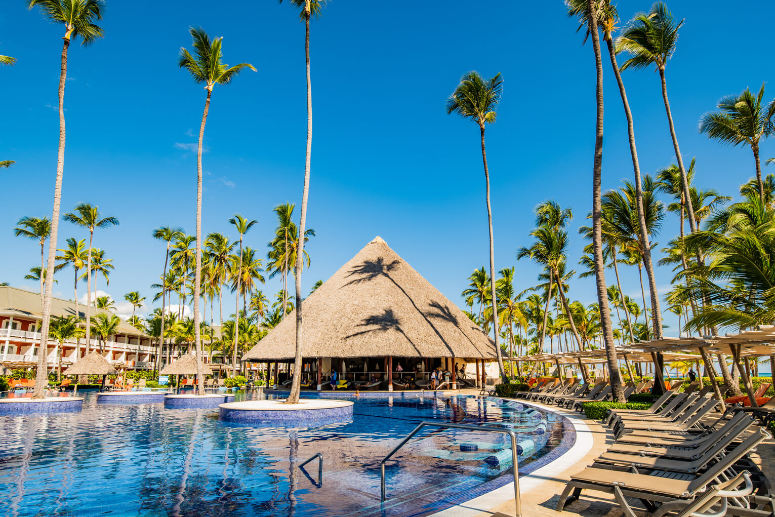 Weihnachten in den Tropen: Resort-Pool mit Palmen, Strohdach-Bar und Liegen unter blauem Himmel