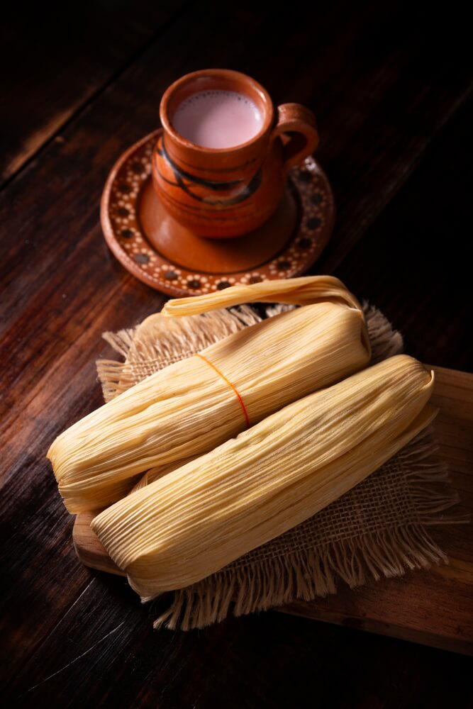 Weihnachten in der Karibik: Tamales auf einem Holzbrett neben einem Tonbecher mit Getränk