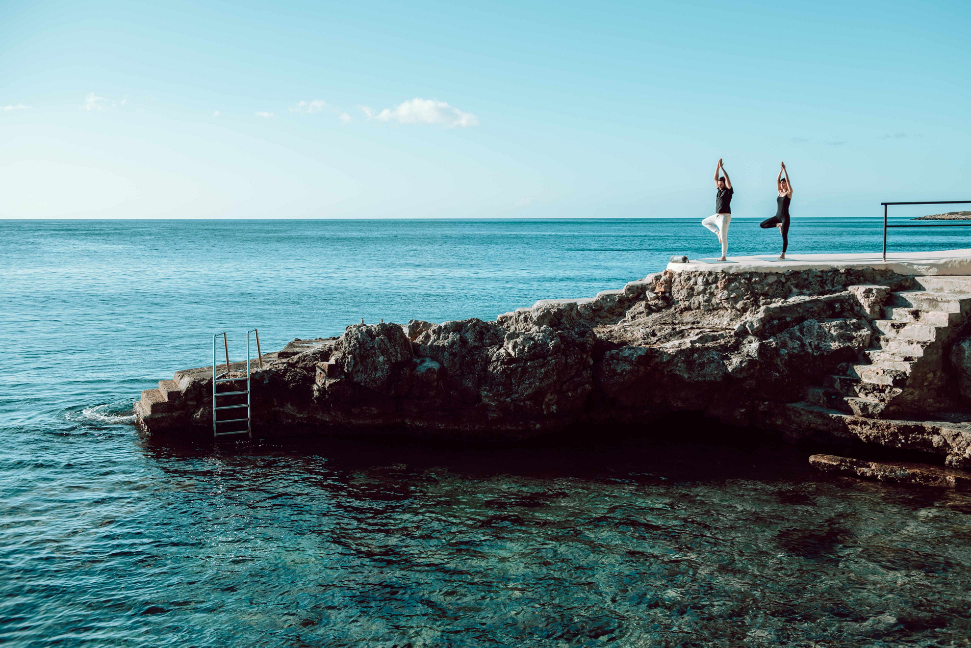 Yoga im Urlaub: ein Paar praktiziert auf einem Felsen am Meer