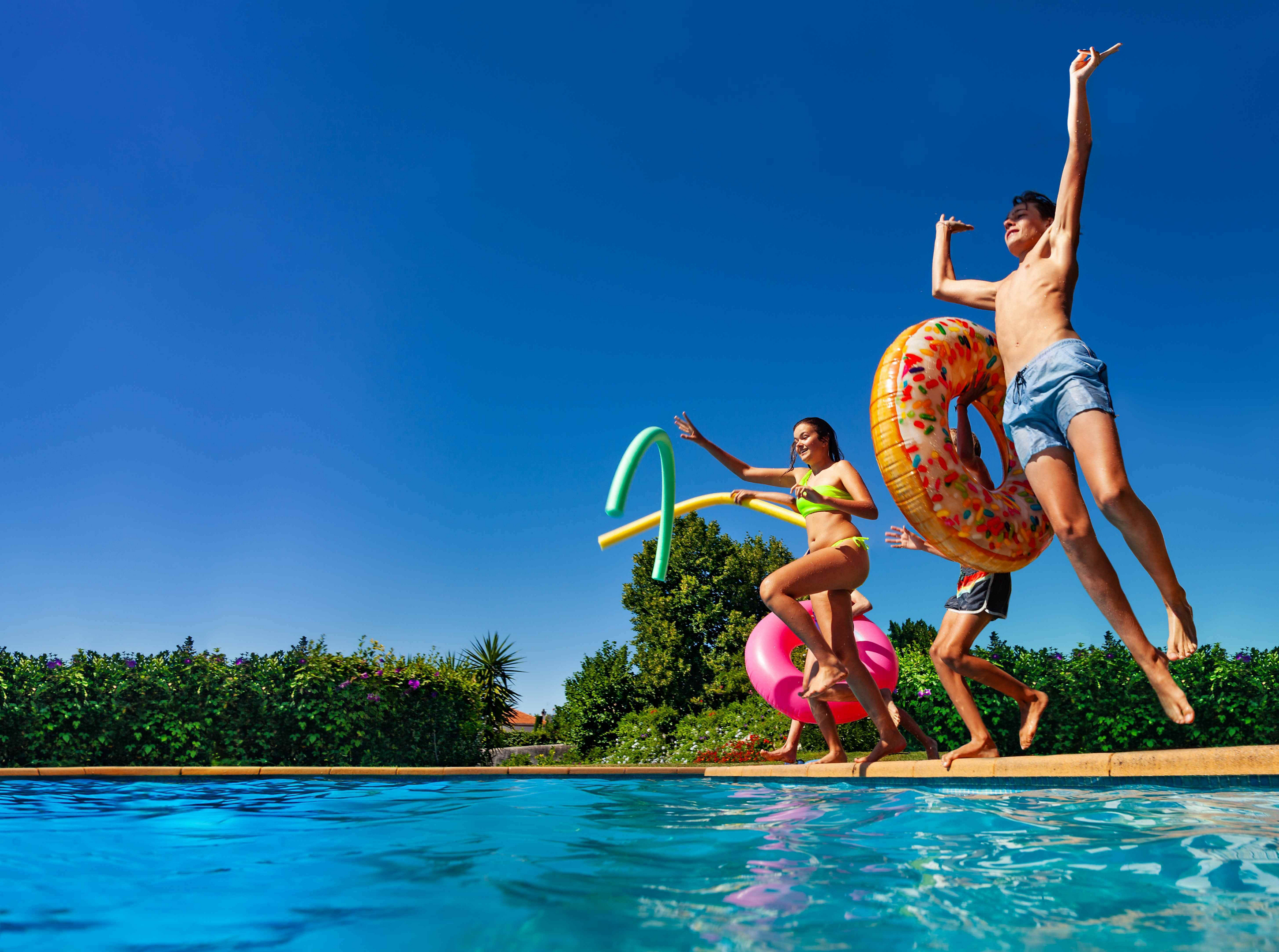 Family resorts: Kids jumping into a pool with colourful inflatables in their hands